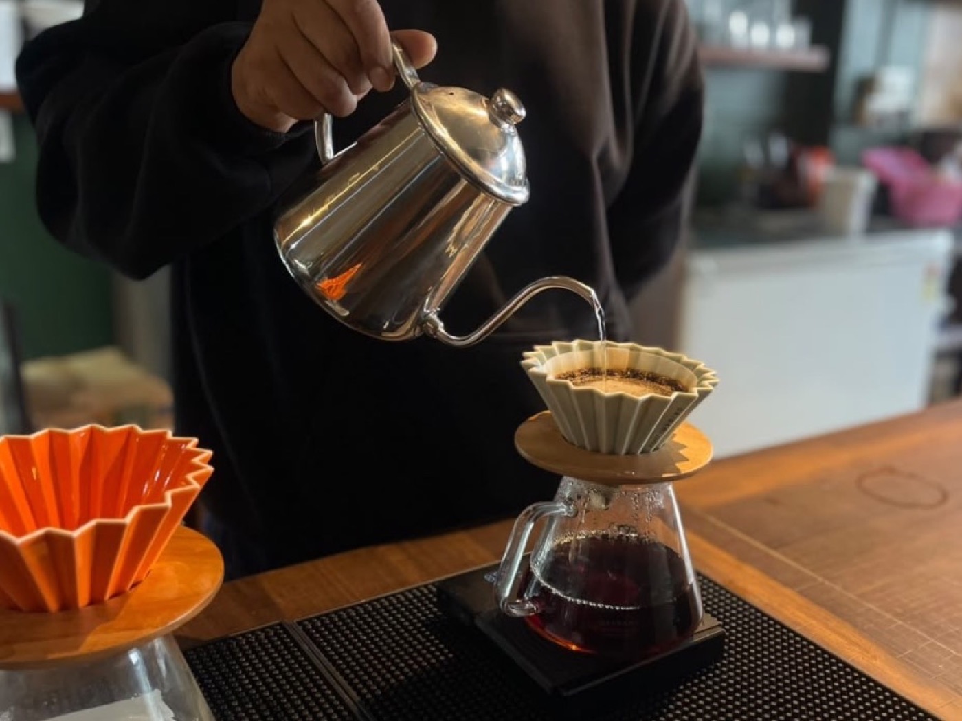 A barista pouring from a gooseneck kettle into an Origami dripper at the Autumn Brew bar